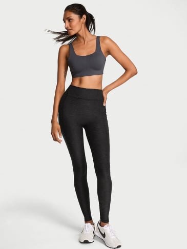 Full body view of a women standing in Victoria's Secret black sport leggings on a light grey backround.