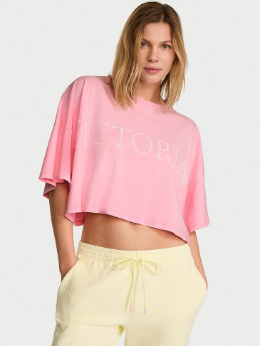 Upper body view of a woman in Victoria's Secret pink Tess and Tanks sport t-shirt on a light grey backround.
